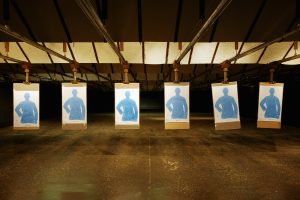 Six blue human-shaped targets hanging from clips in a dim indoor shooting range.