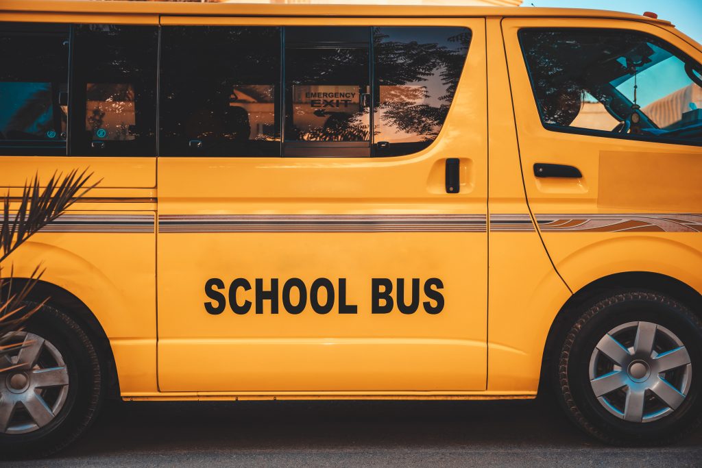 Yellow school bus seen from the side, with the words 'SCHOOL BUS' on the door area and reflections in the windows