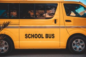 Yellow school bus seen from the side, with the words 'SCHOOL BUS' on the door area and reflections in the windows