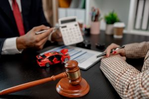 Gavel on a dark desk with a blurred background of a person in a suit, a calculator, and a red toy car on the desk—legal work scene.