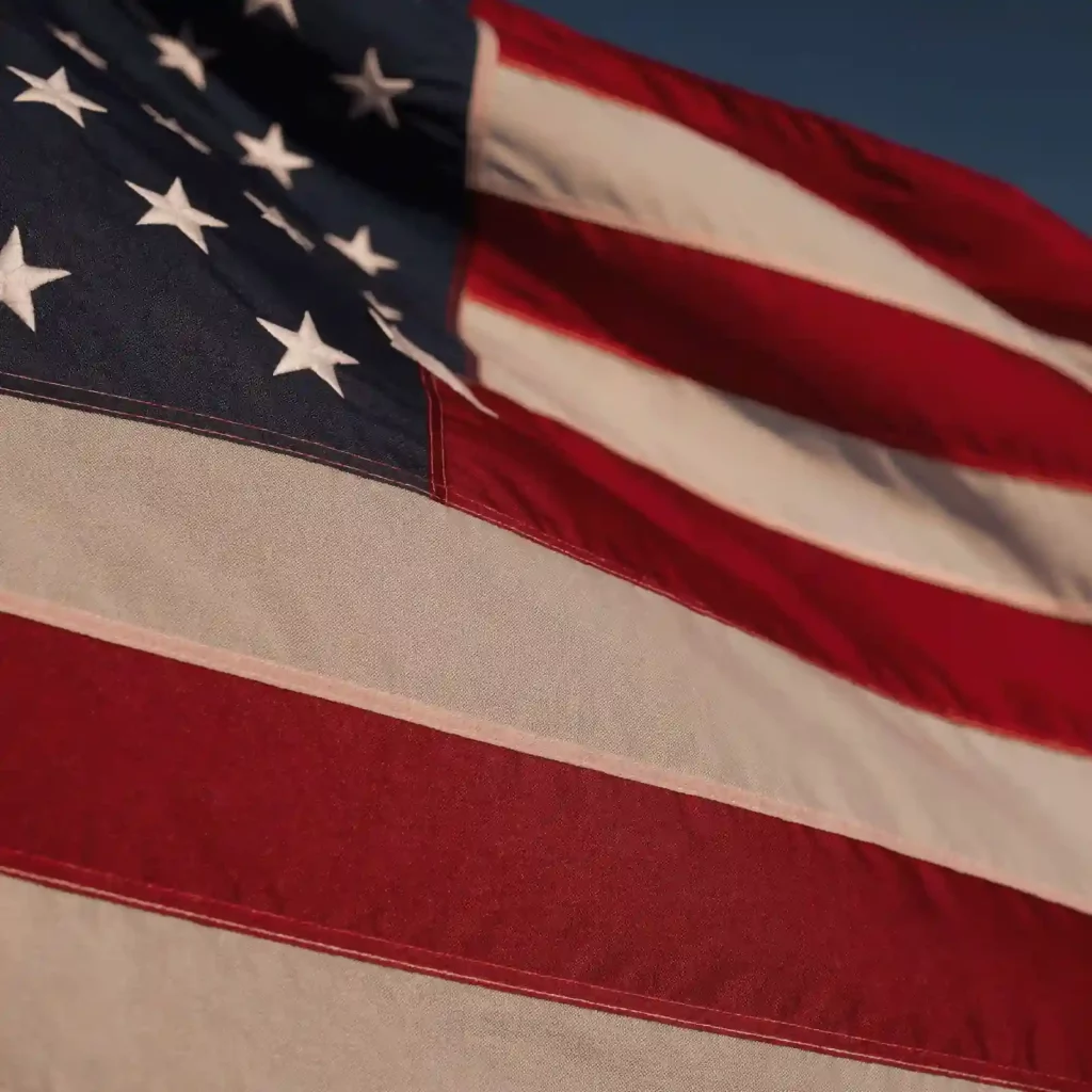 Close-up of the American flag waving, showing white stars on blue and red-and-white stripes in sunlight.