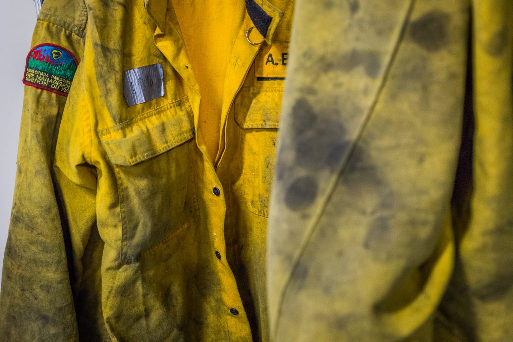Close-up of a dusty yellow firefighter turnout jacket with a red armband patch on the left sleeve.