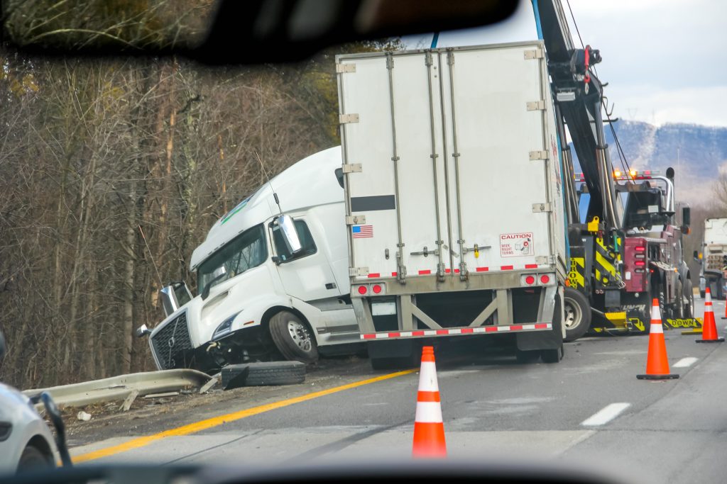 White semi-truck jackknifed on the highway with debris and orange traffic cones nearby